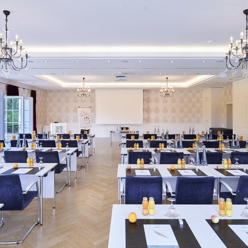 Der Tagungsraum Auerberg Diamant in Konferenzbestuhlung mit eingedeckten Tischen für die Teilnehmer mit Blick zur Leinwand.