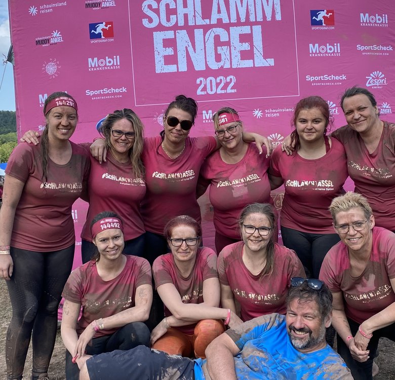 Teamaufstellung nach dem Run mit schlammiger Kleidung und erschöpften Gesichtern vor dem Logobanner des Events.