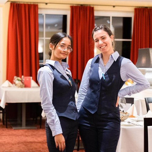 Zwei Servicemitarbeiterinnen stehen lächelnd im Restaurant Waldteufel im Schindelbruch an einem Tisch gelehnt.